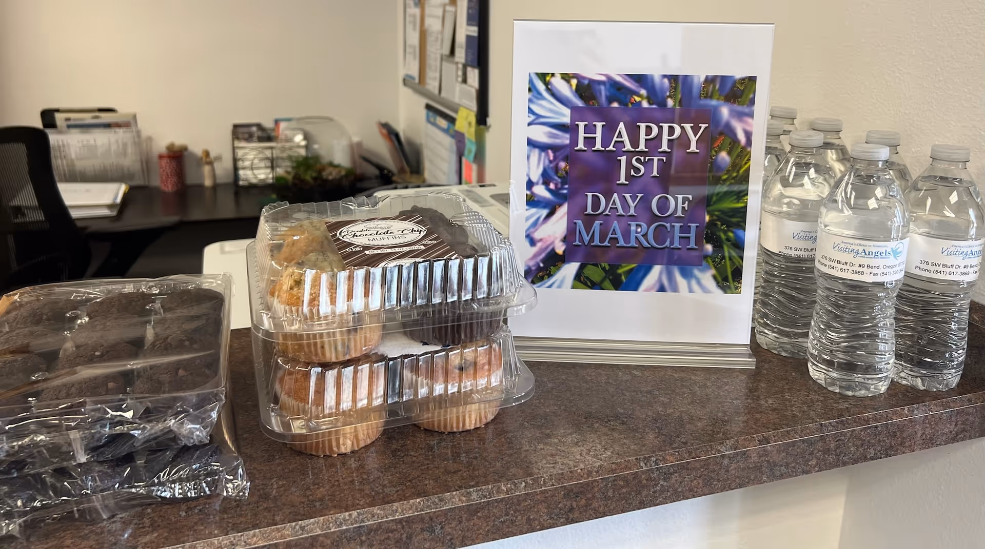 A counter displays cupcakes, water bottles, and a Happy 1st Day of March sign.