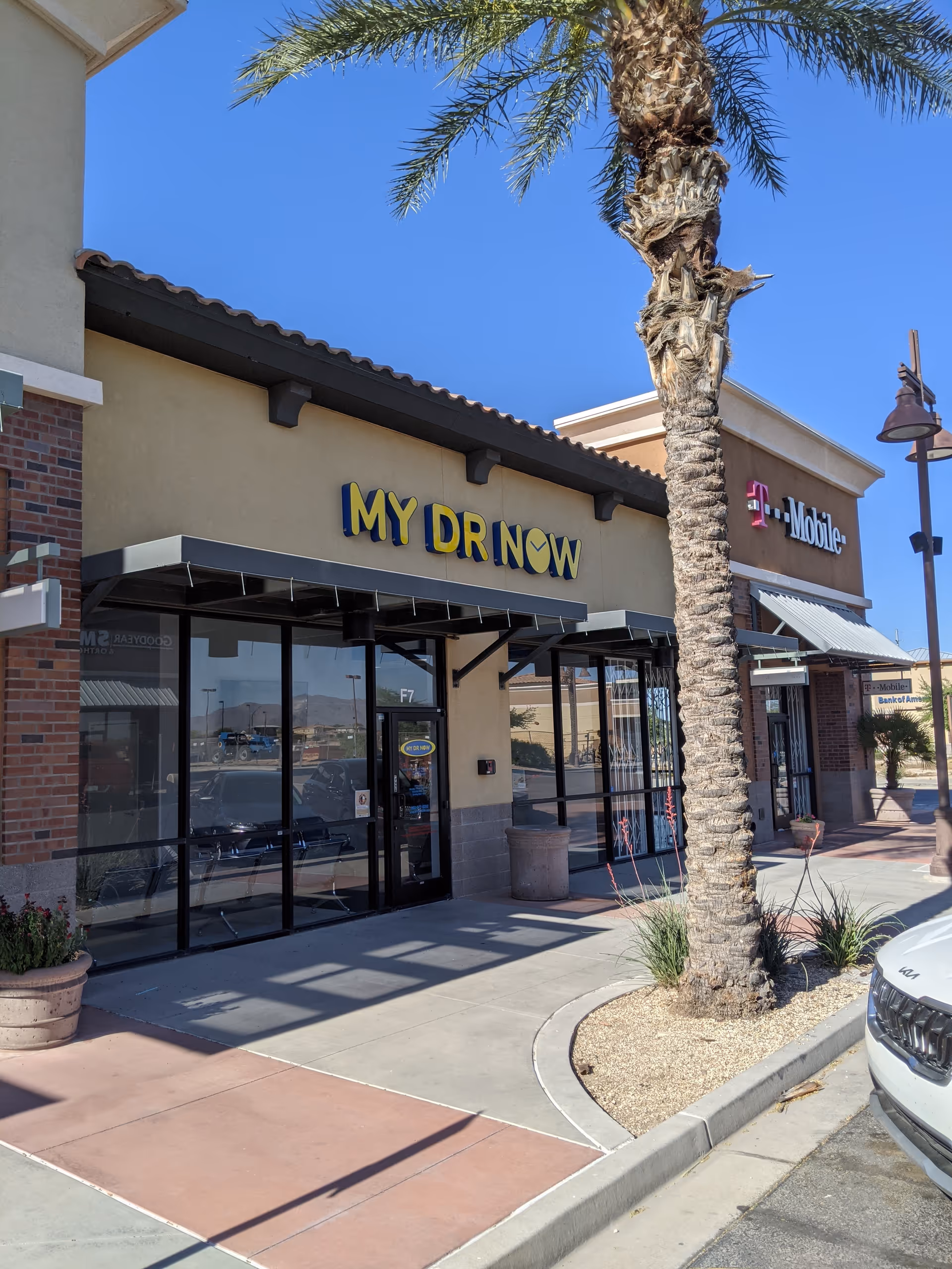 Exterior view of a shopping plaza with MY DR NOW, T-Mobile storefronts, and palm tree.