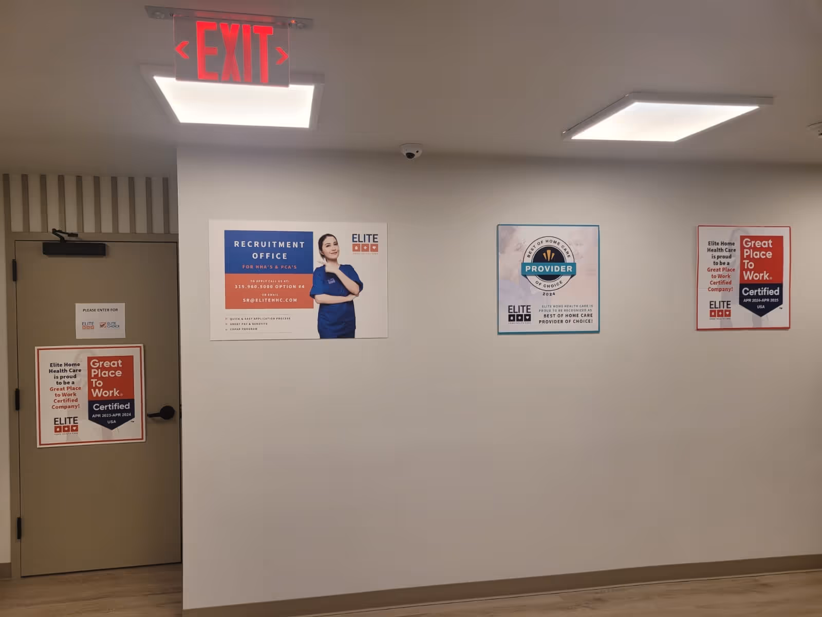 Interior hallway of Elite Home Health Care with exit sign, posters, and a door.