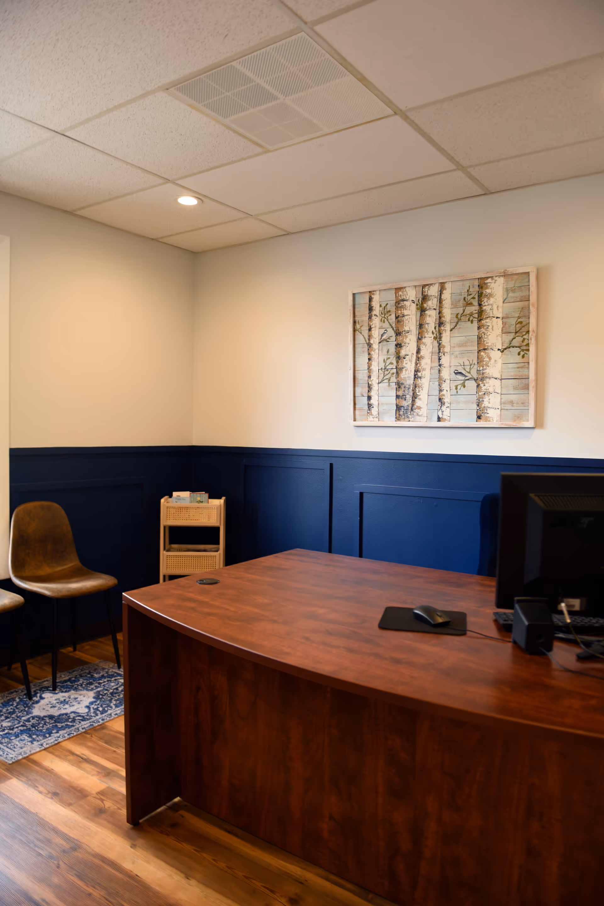 A wooden reception desk in a blue-walled office area with birch-tree artwork.