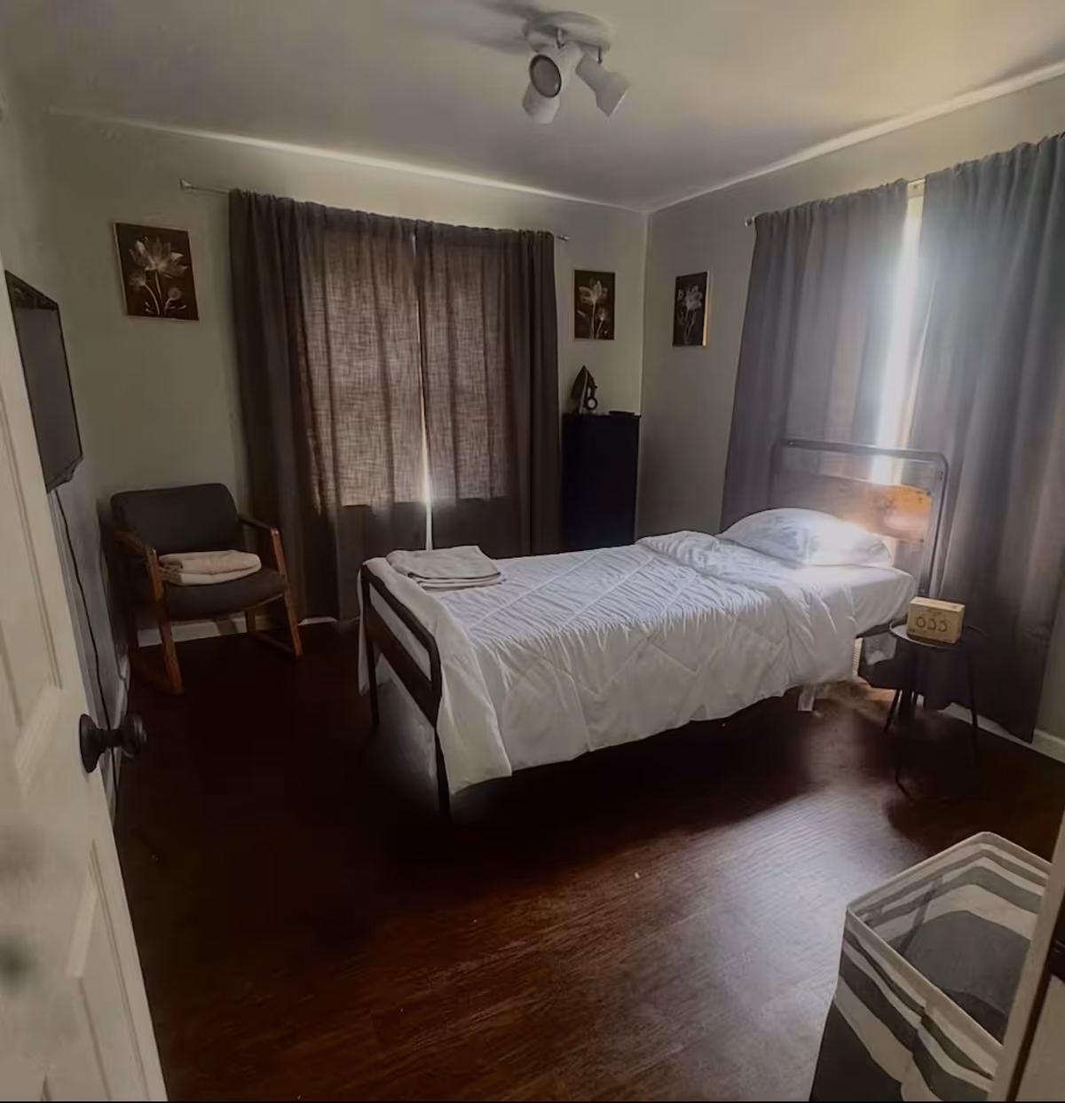A small bedroom with a single bed, dark curtains, chair, and dresser.