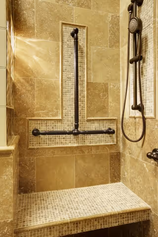 Taupe tiled bathroom shower featuring built-in seating and grab bars.