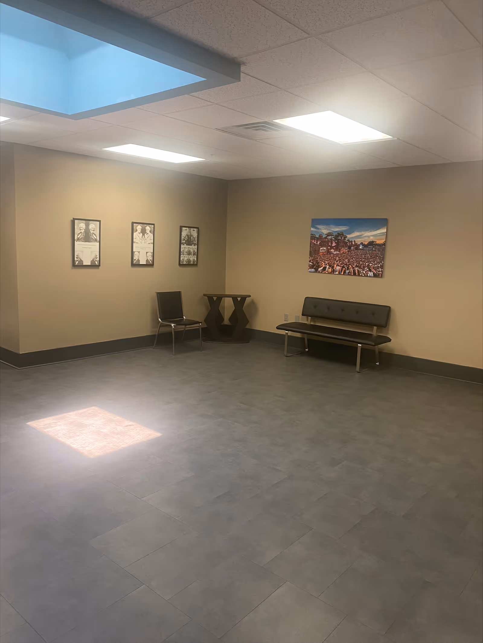 An empty waiting area with chairs, a bench, and wall art in a neutral-toned room.