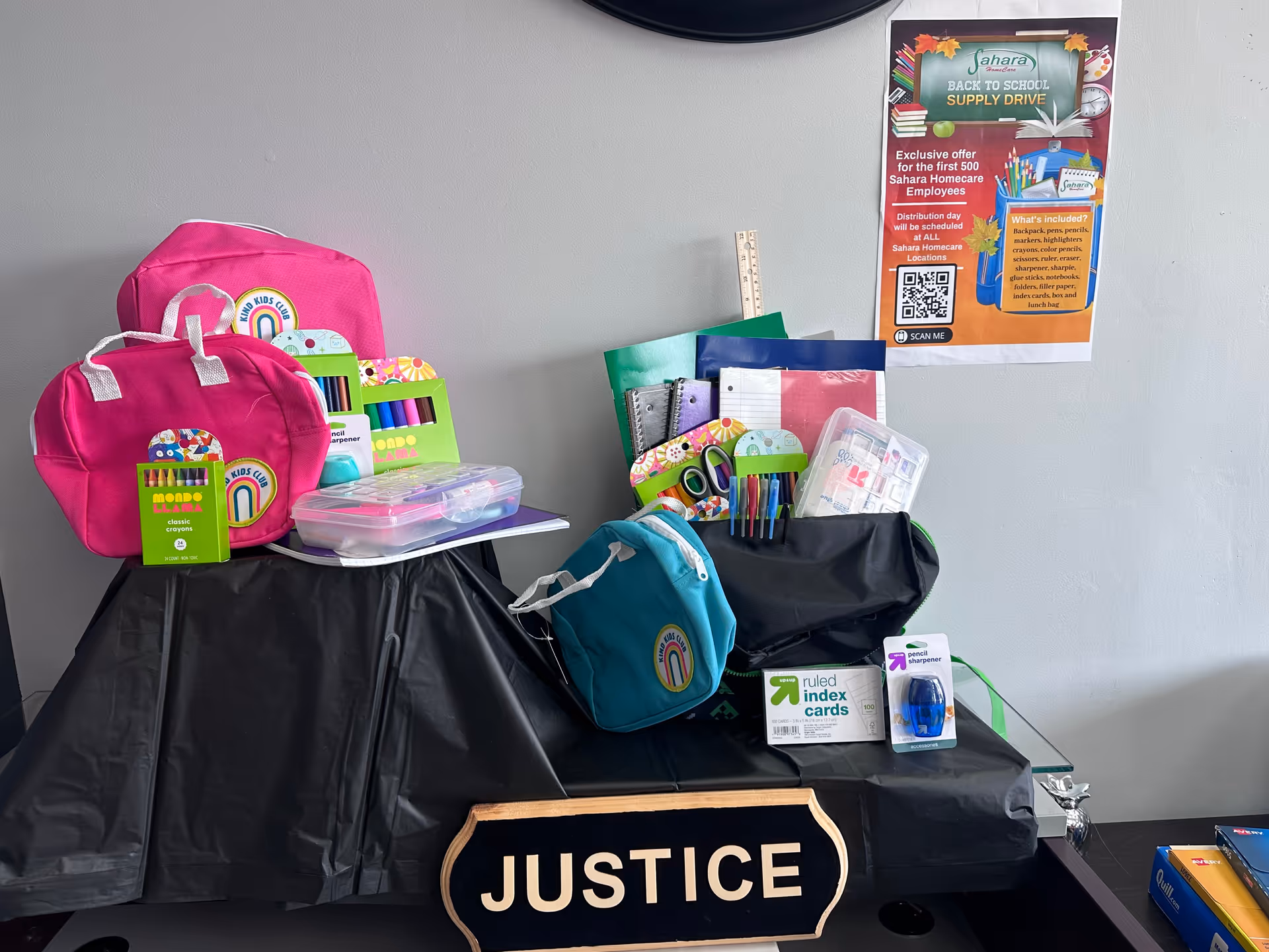Table displays colorful school supplies and a Justice sign in an indoor setting.