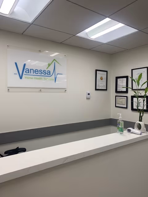 Reception desk with Vanessa Home Health Services sign, framed certificates, plant, and hand sanitizer.