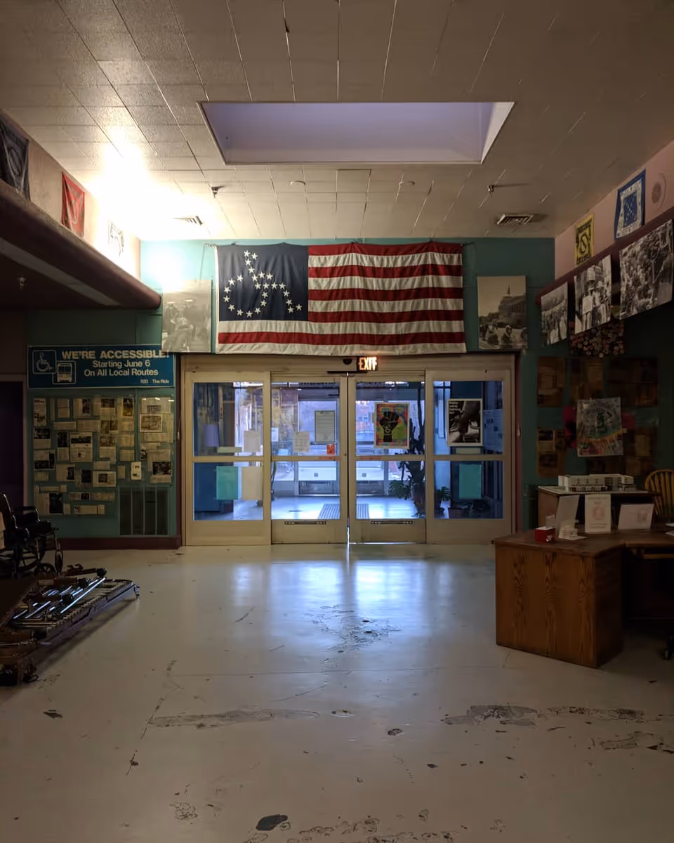 Dim interior lobby with glass doors, a flag banner, and bulletin boards.