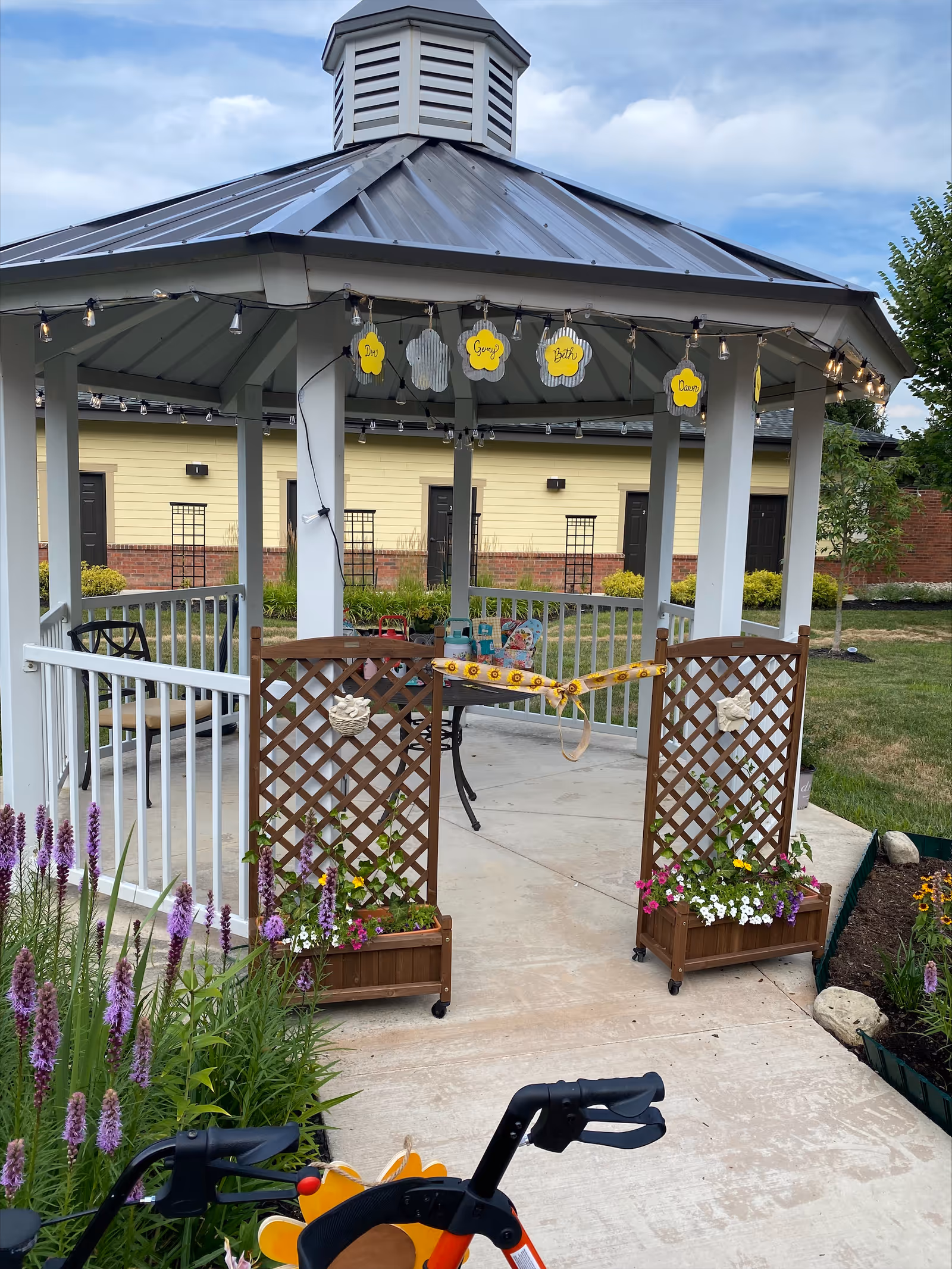 Outdoor gazebo with string lights and planters at a senior living facility.
