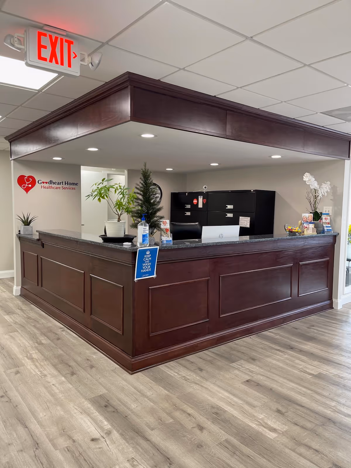 Wooden reception counter in a bright Goodheart Home Healthcare lobby with plants.