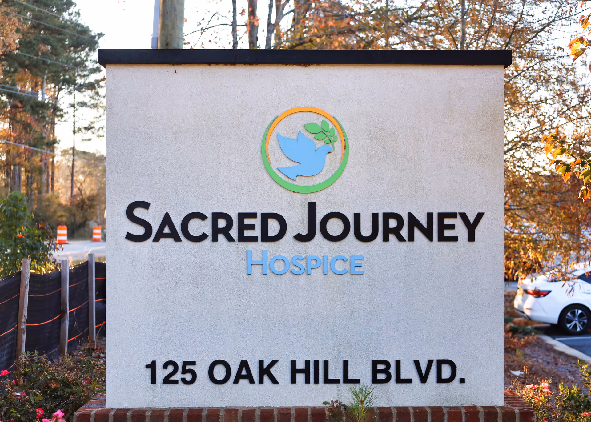A large exterior sign reads Sacred Journey Hospice with logo and 125 Oak Hill Blvd.