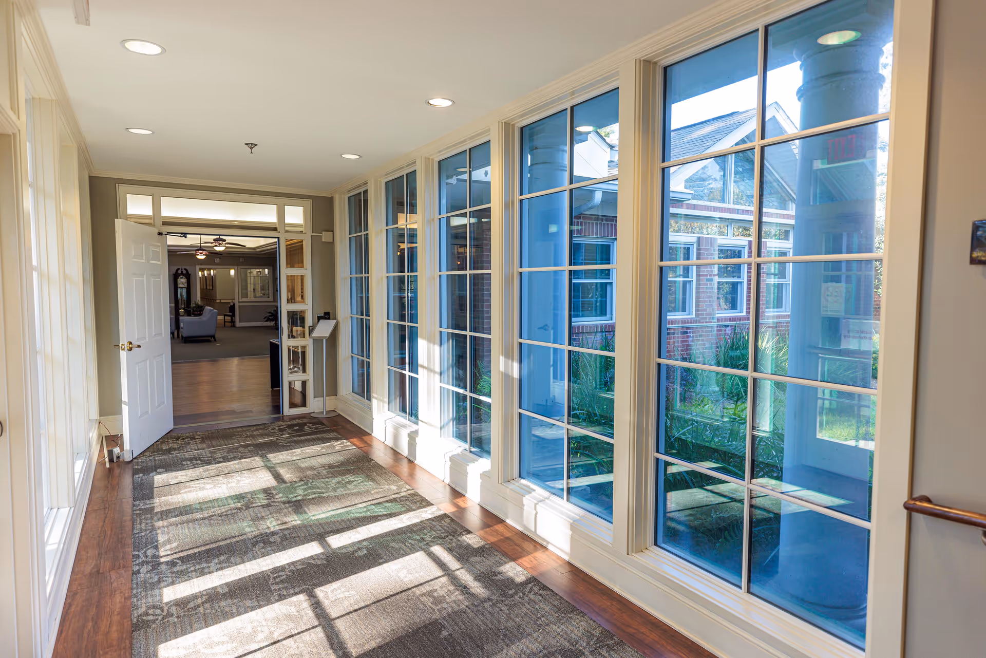 Bright hallway with large windows along one side and a doorway leading to a seating area.