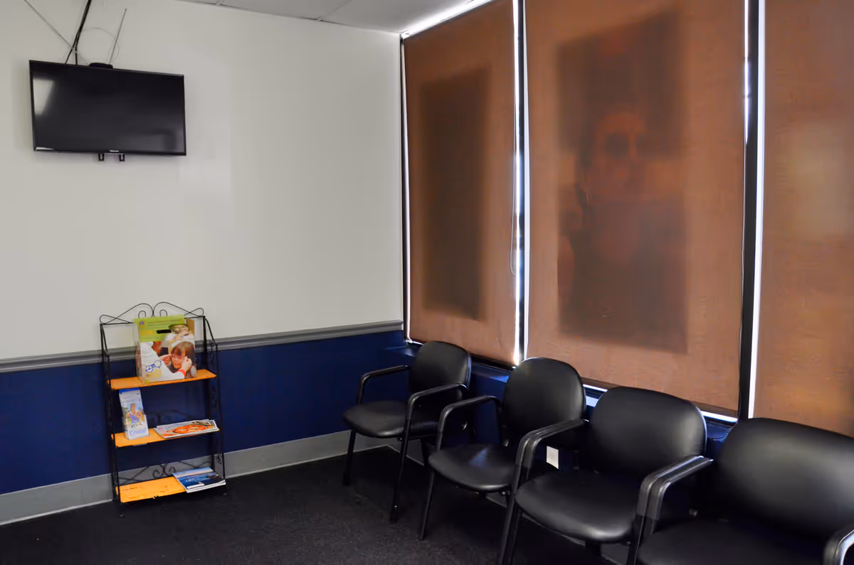 Waiting area with black chairs, a wall-mounted TV, and brochure rack.