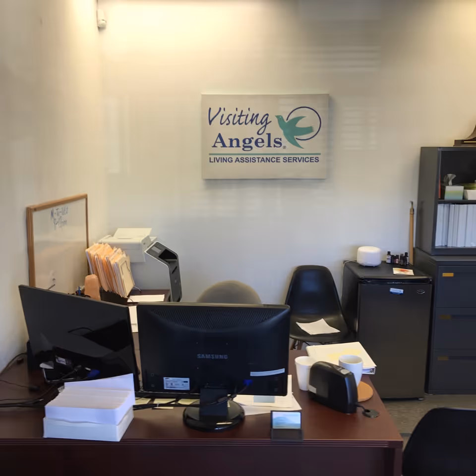 Reception desk with computer and a Visiting Angels sign on the wall.