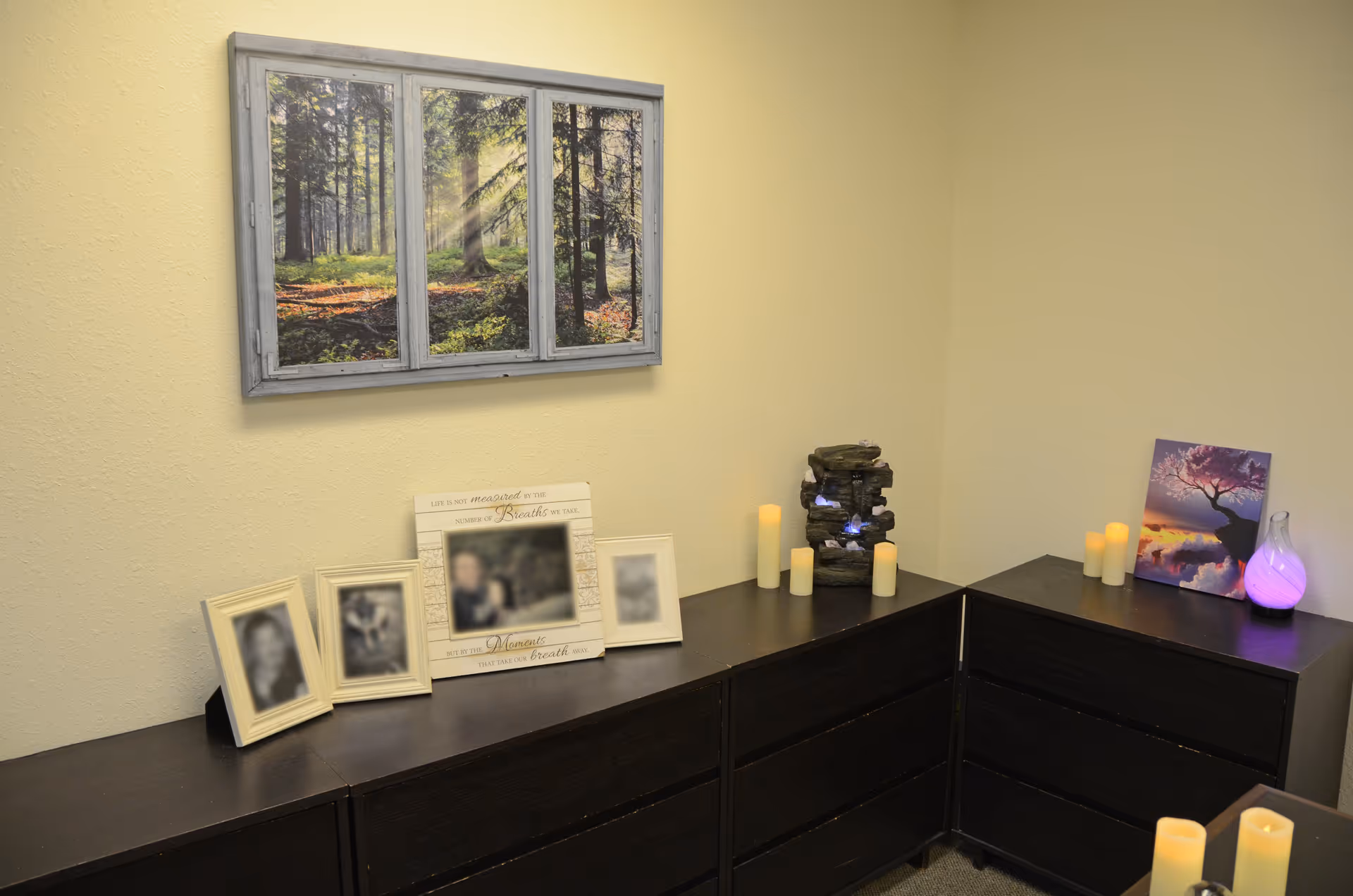 Corner of a beige room with dark cabinets, framed photos, candles, and wall art.