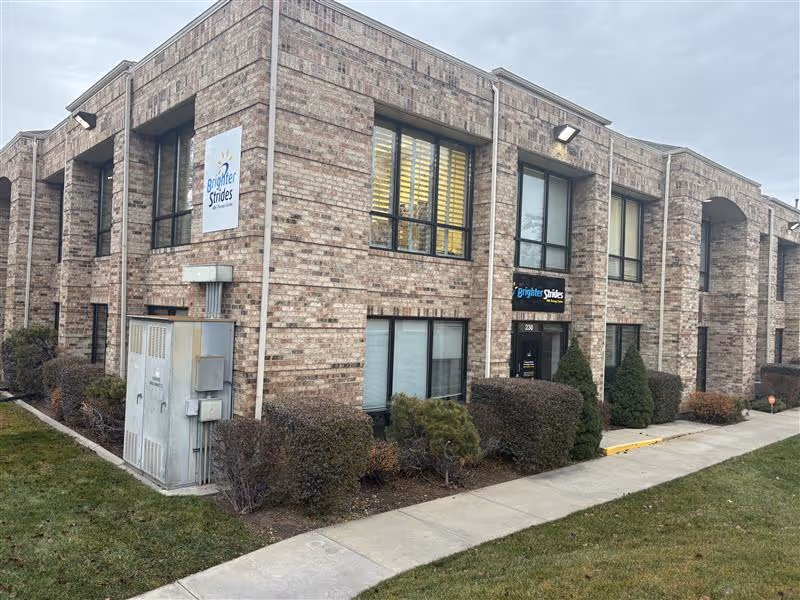 Brick exterior of Brighter Strides ABA Therapy building with windows and trimmed shrubs.