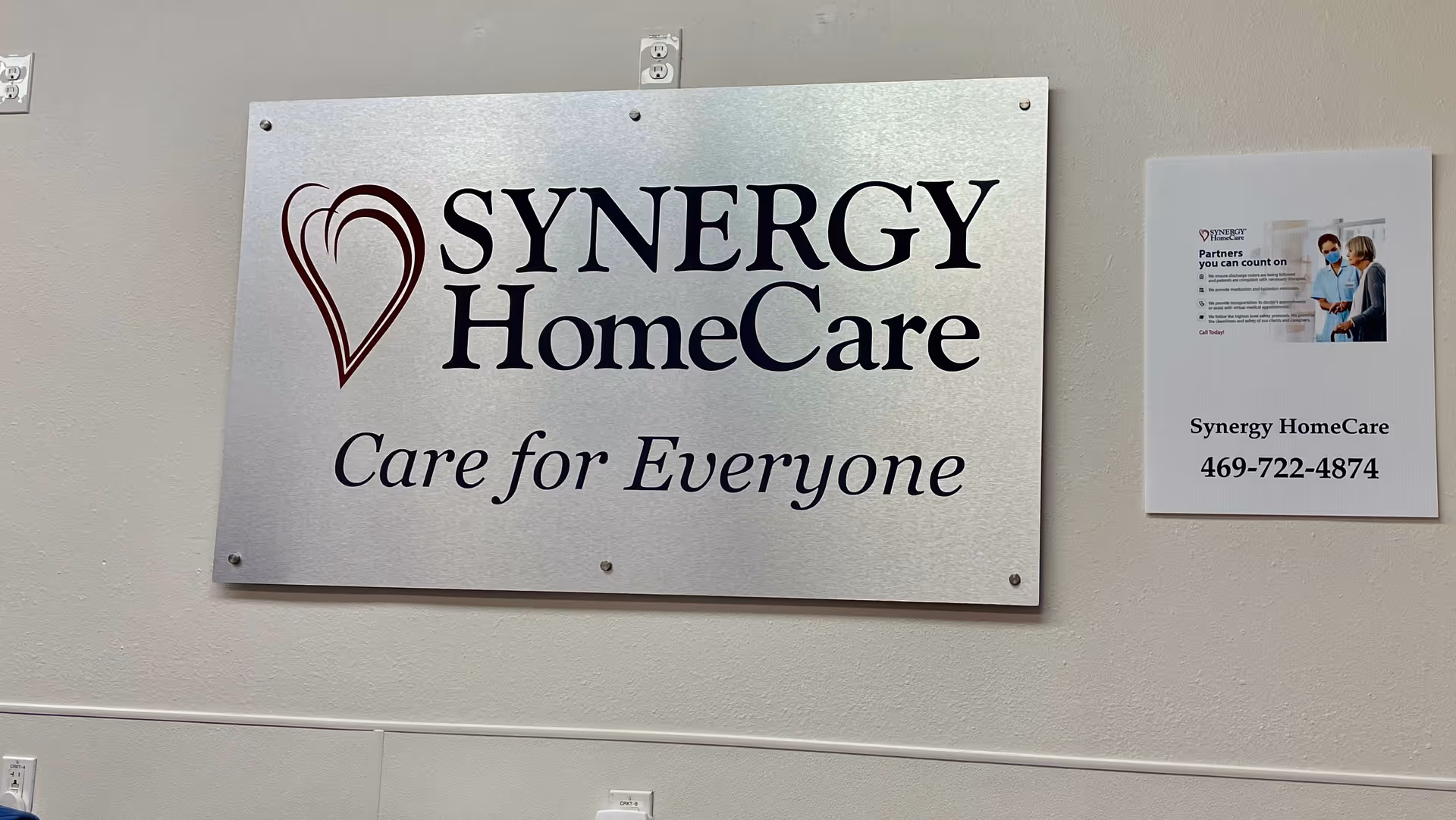 Metal SYNERGY HomeCare sign with 'Care for Everyone' on an interior wall.