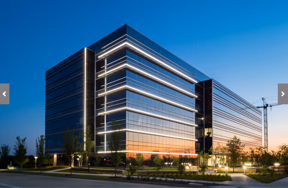 Modern glass office building exterior at dusk with illuminated horizontal light bands.