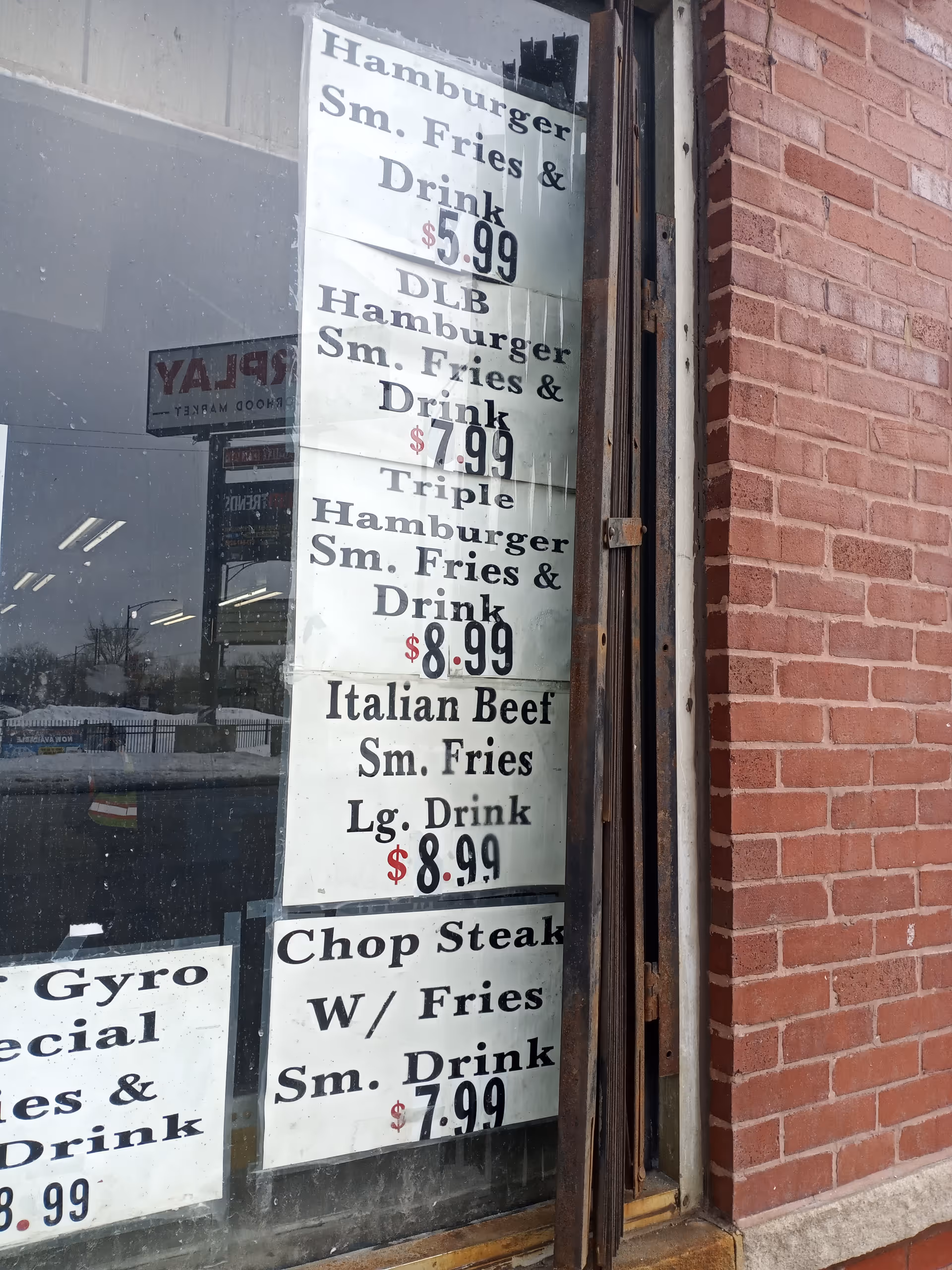 Brick storefront window with white menu signs listing hamburgers, fries, and drinks.