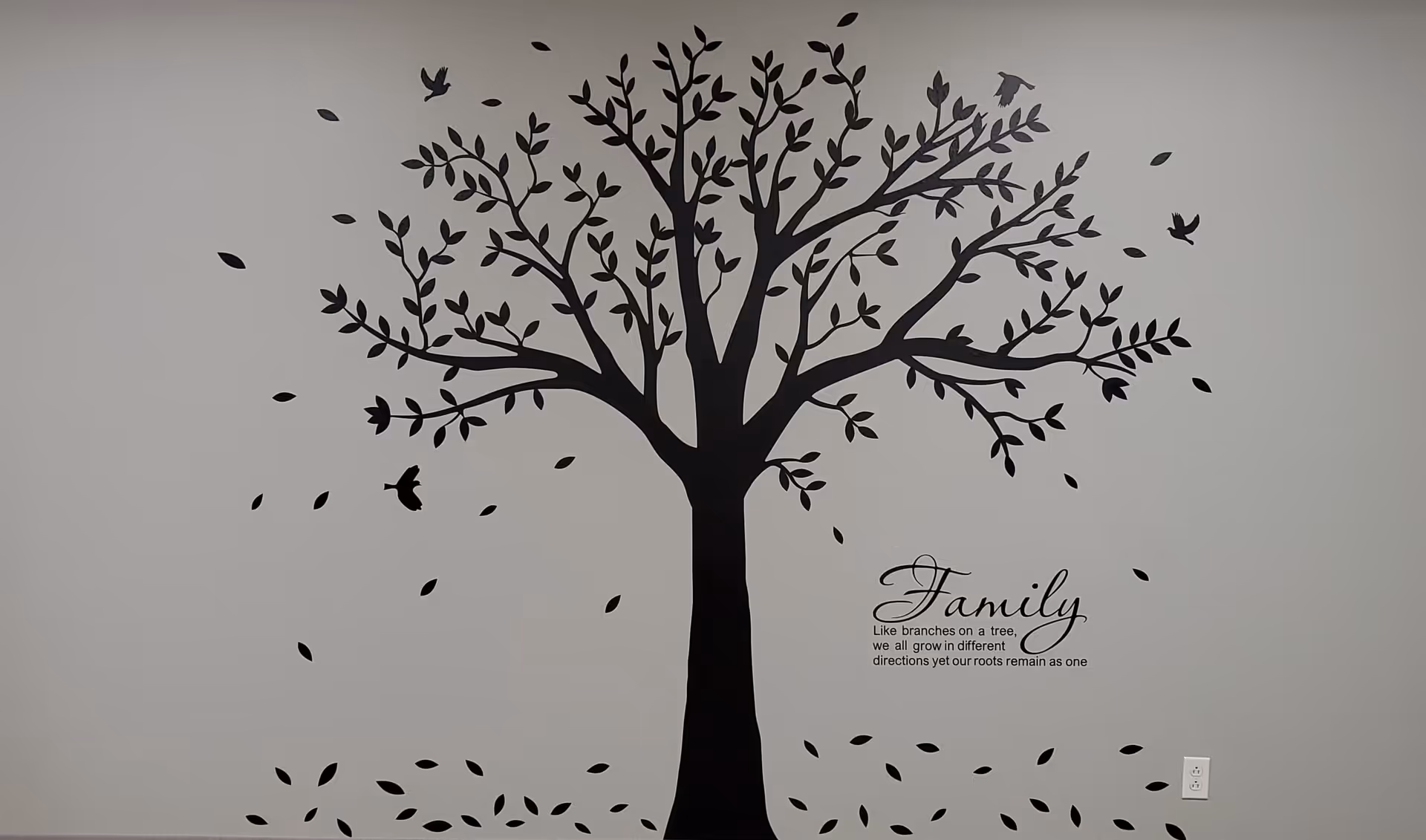 Large black tree mural with falling leaves on a light gray wall