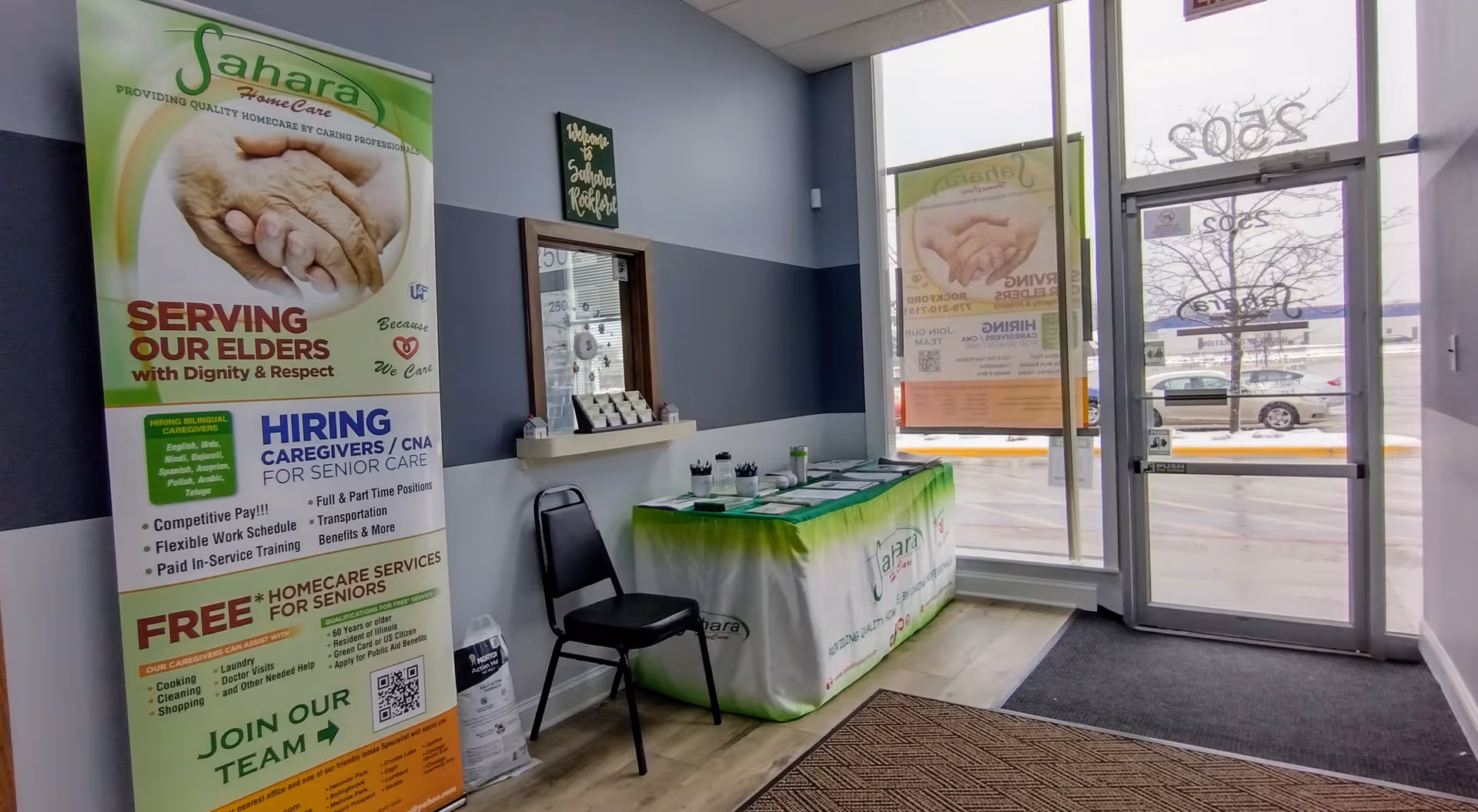 Lobby interior of Sahara Home Care with banners, a reception table, and glass doors.