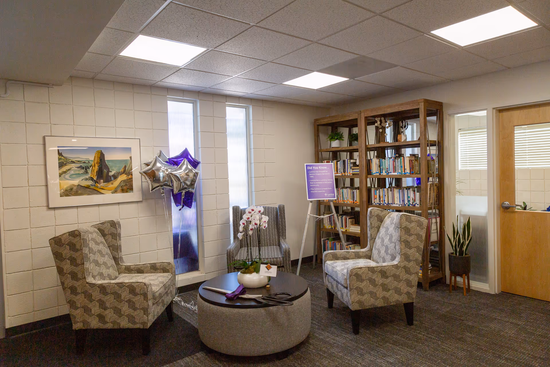 A cozy lounge area with patterned chairs, a round coffee table, and a tall bookshelf.