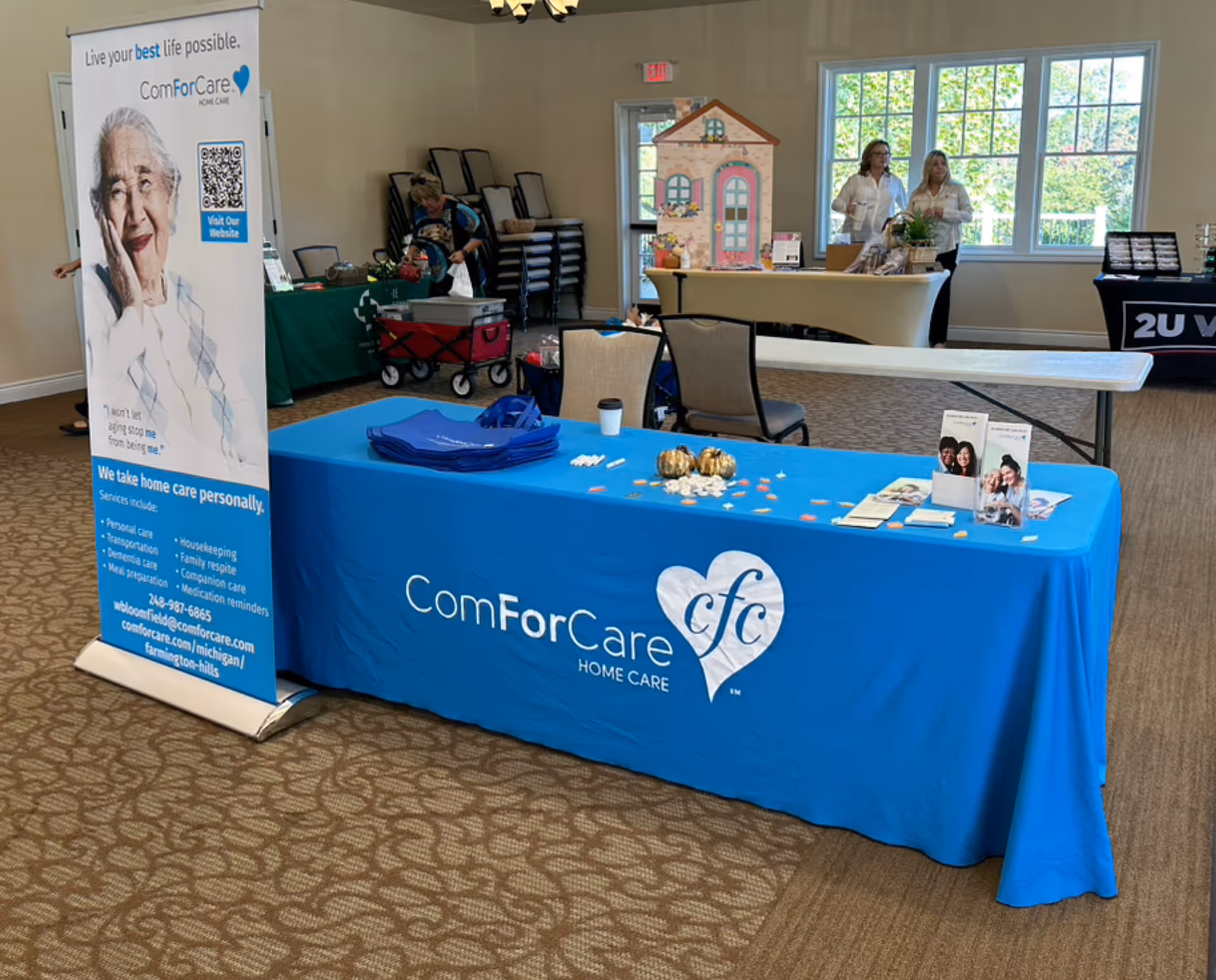 Indoor event booth for ComForCare with blue table and banner, surrounded by attendees.