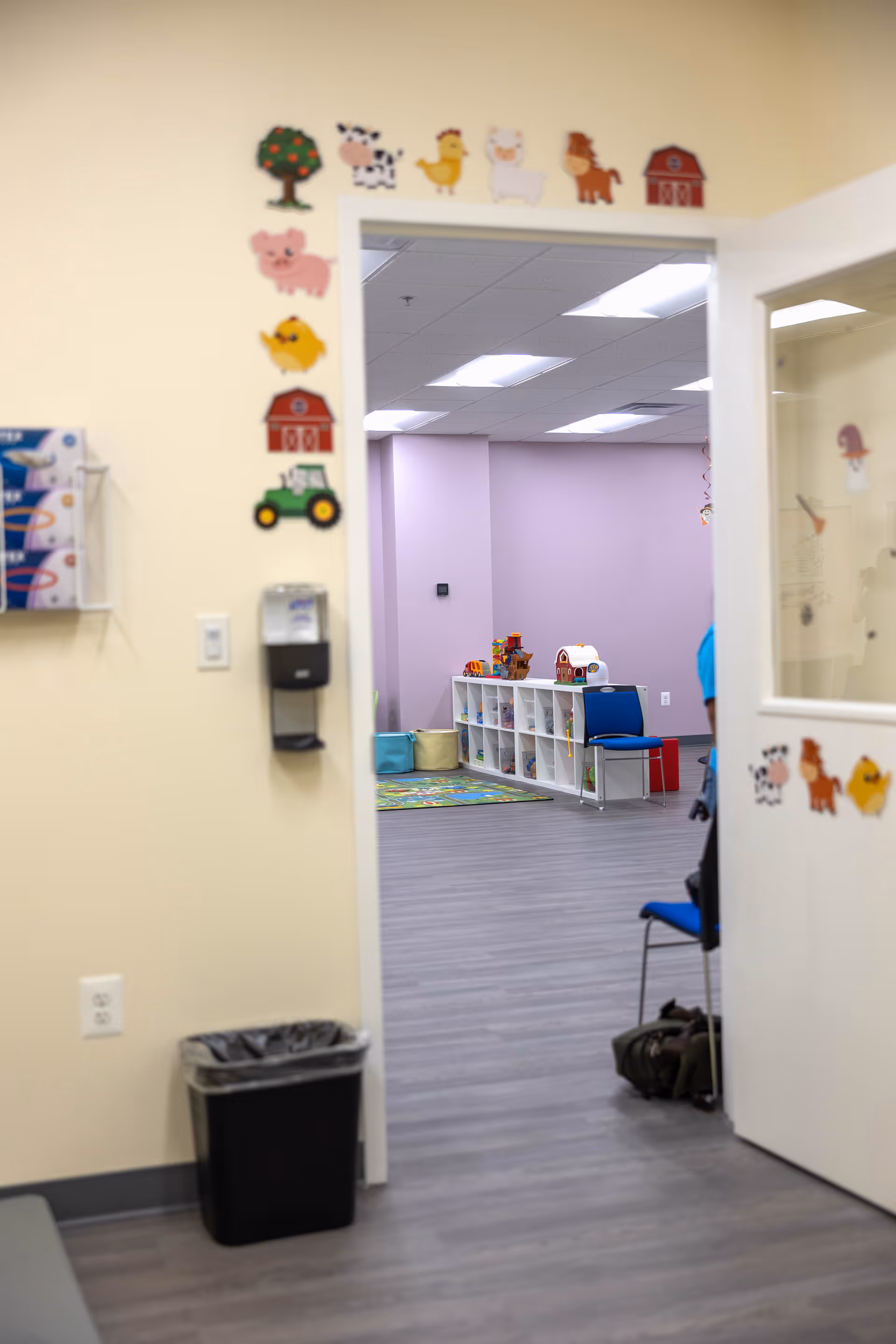 Doorway to a colorful pediatric playroom with shelves, toys, and soft mats.
