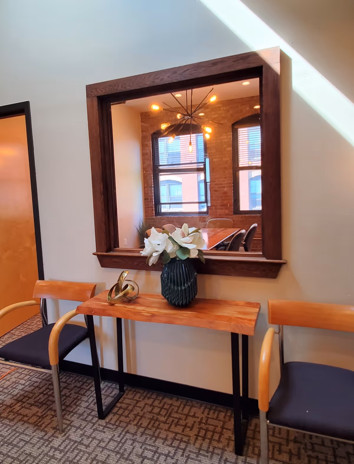 Wood console with vase and two chairs in a hallway with a large mirror.
