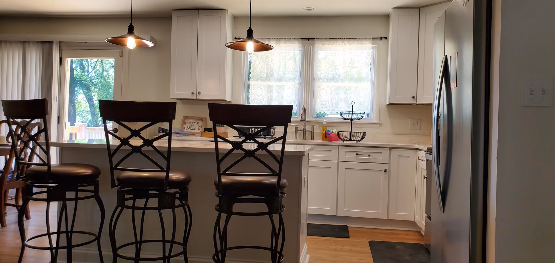 Bright kitchen area with white cabinets, bar stools, and a stainless refrigerator.