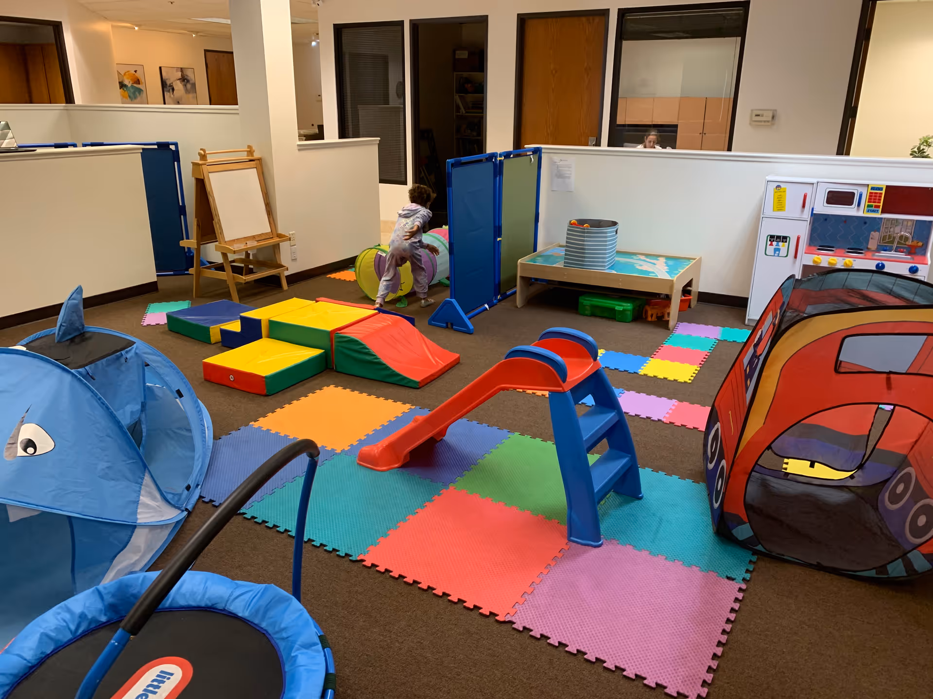 A child playing in a colorful indoor playroom with foam mats and play equipment