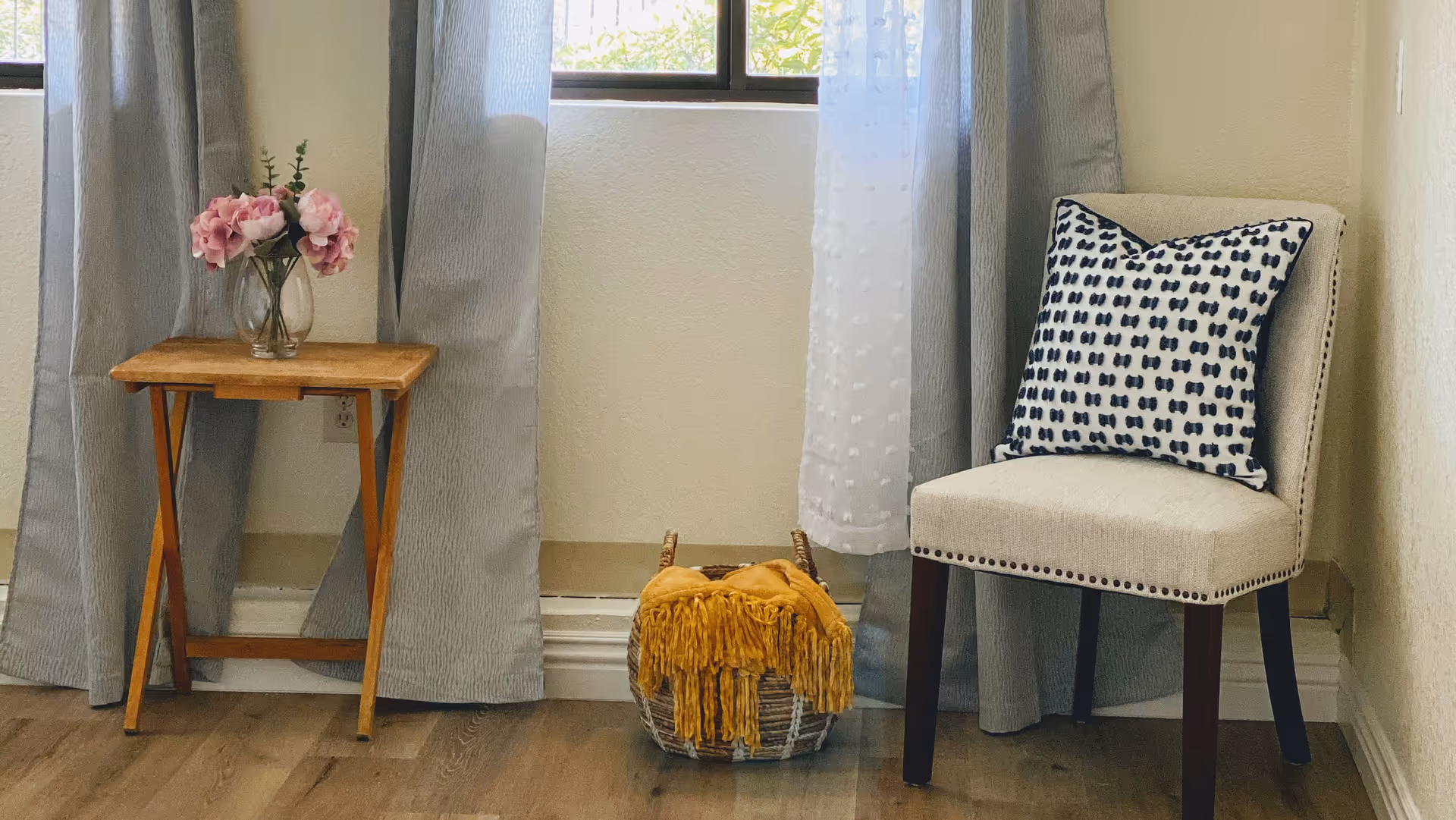 Cozy seating nook with a wooden table, pink flowers, and a cushioned chair.