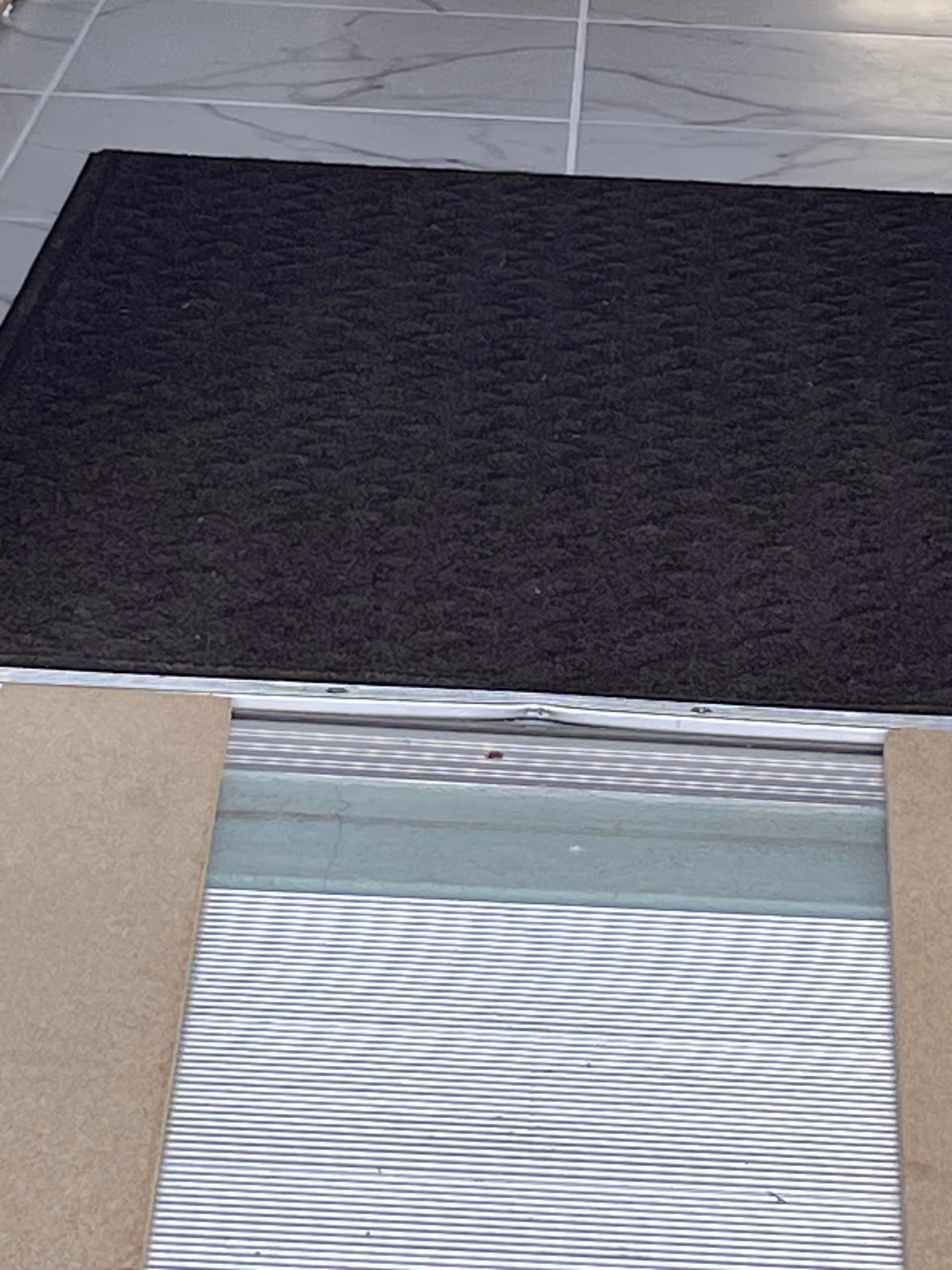 Close-up view of a doorway threshold with a dark entry mat on tiled floor.