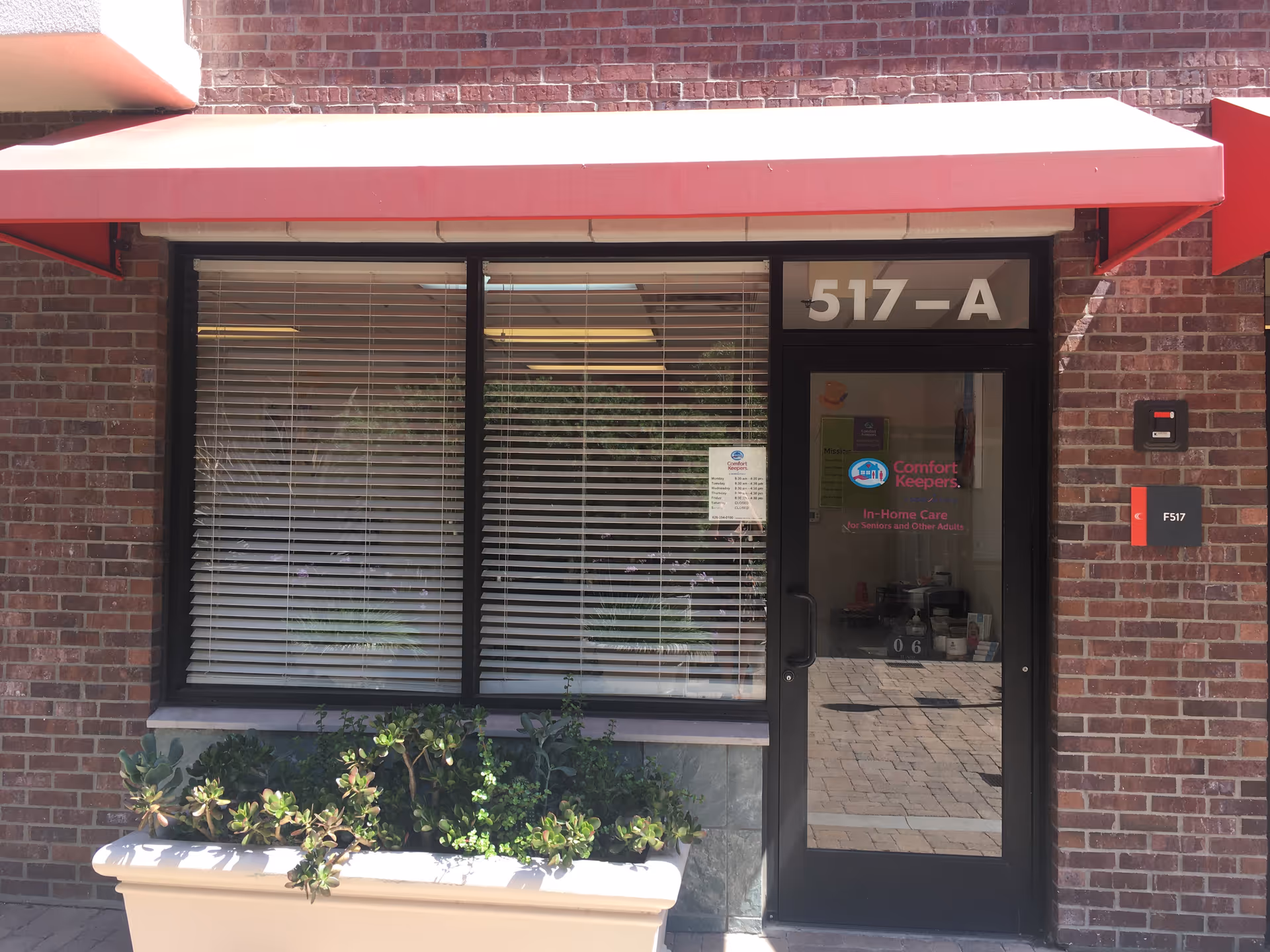 Brick storefront exterior with a red awning, blinds, and a glass door labeled Comfort Keepers.