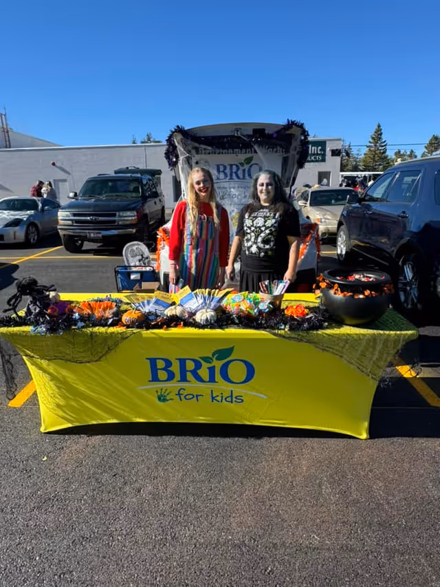 Two women stand behind a BRiO for kids table at an outdoor event.