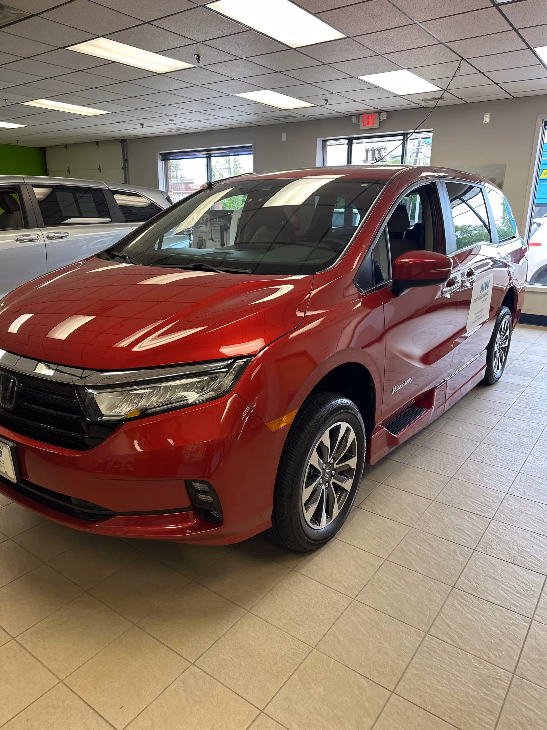 Red minivan on display inside a showroom with tiled floor and ceiling lights.