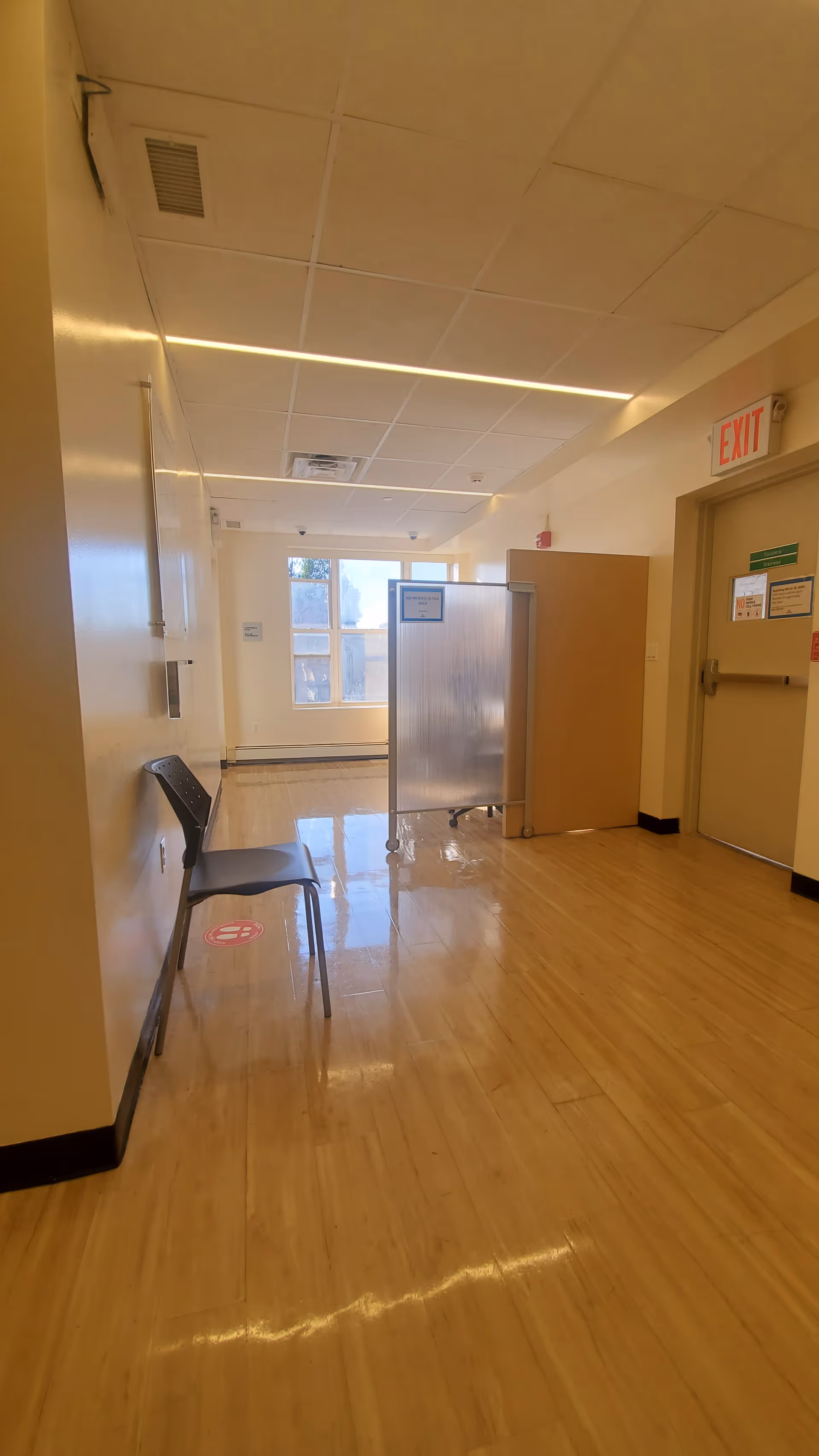 Long indoor hallway in facility with folding partition, chairs, and exit door.