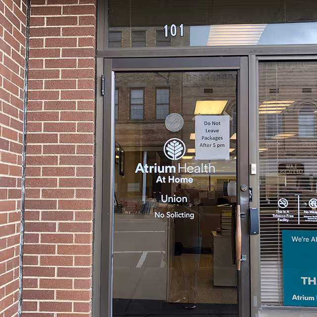 Brick building entrance with glass door displaying Atrium Health At Home Union signage.