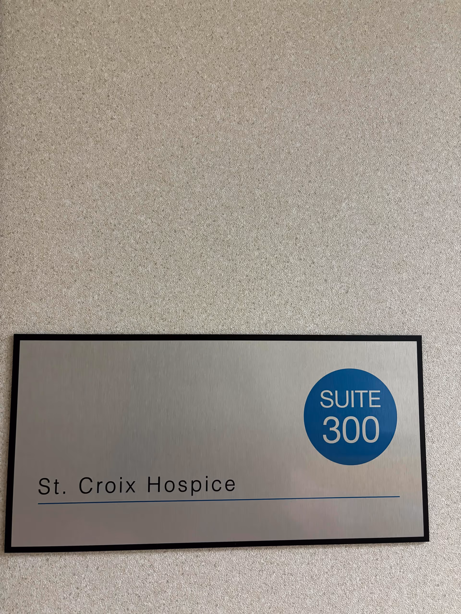 A metal sign on a textured wall reading St. Croix Hospice, Suite 300.