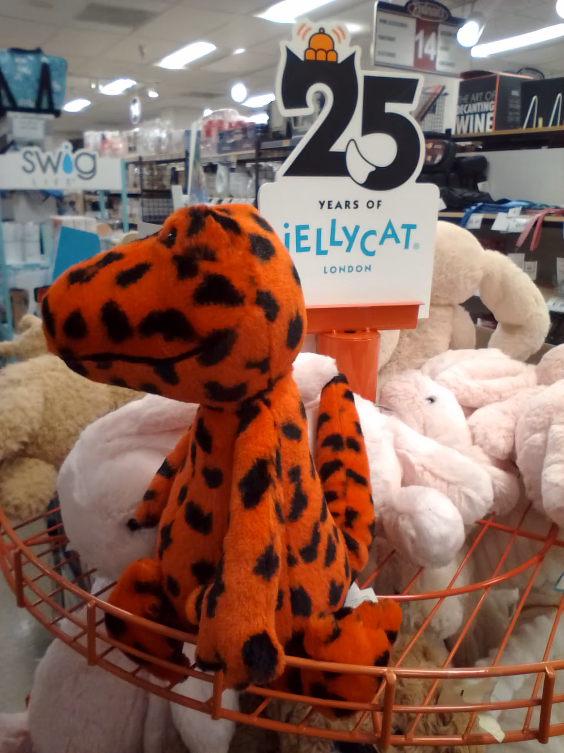 Orange plush tiger with black spots sits in a basket among stuffed animals in a store.