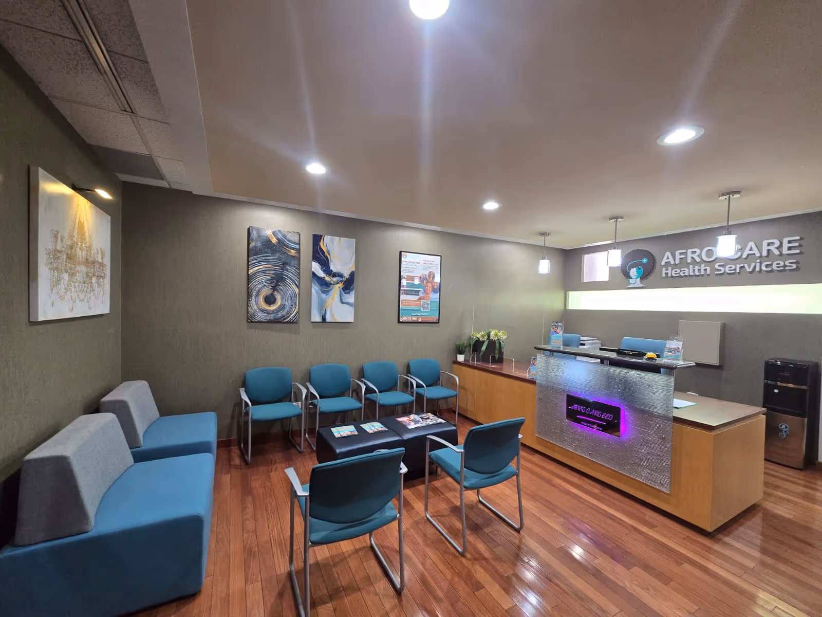 A facility lobby with blue chairs, a reception desk, and wall art.