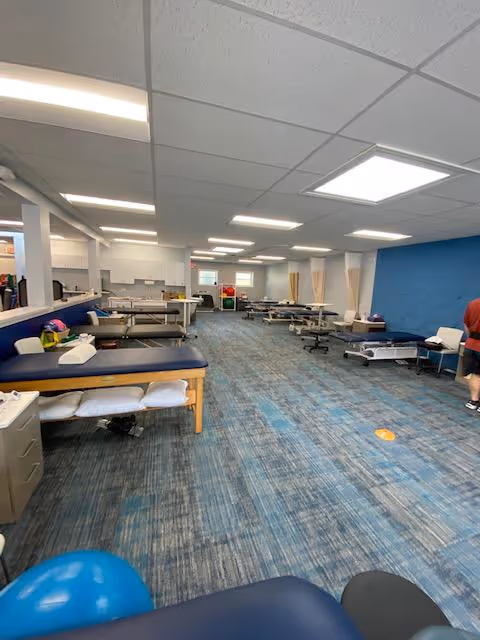 Long rehabilitation therapy room with multiple treatment tables and blue decor.