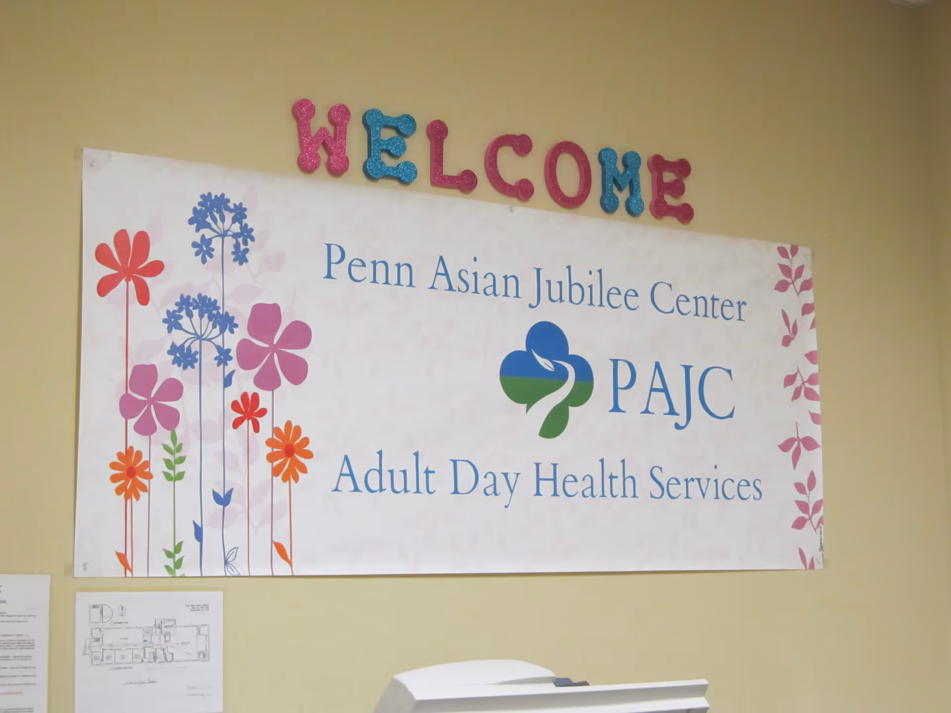 Welcome sign above PAJC poster on a yellow interior wall.