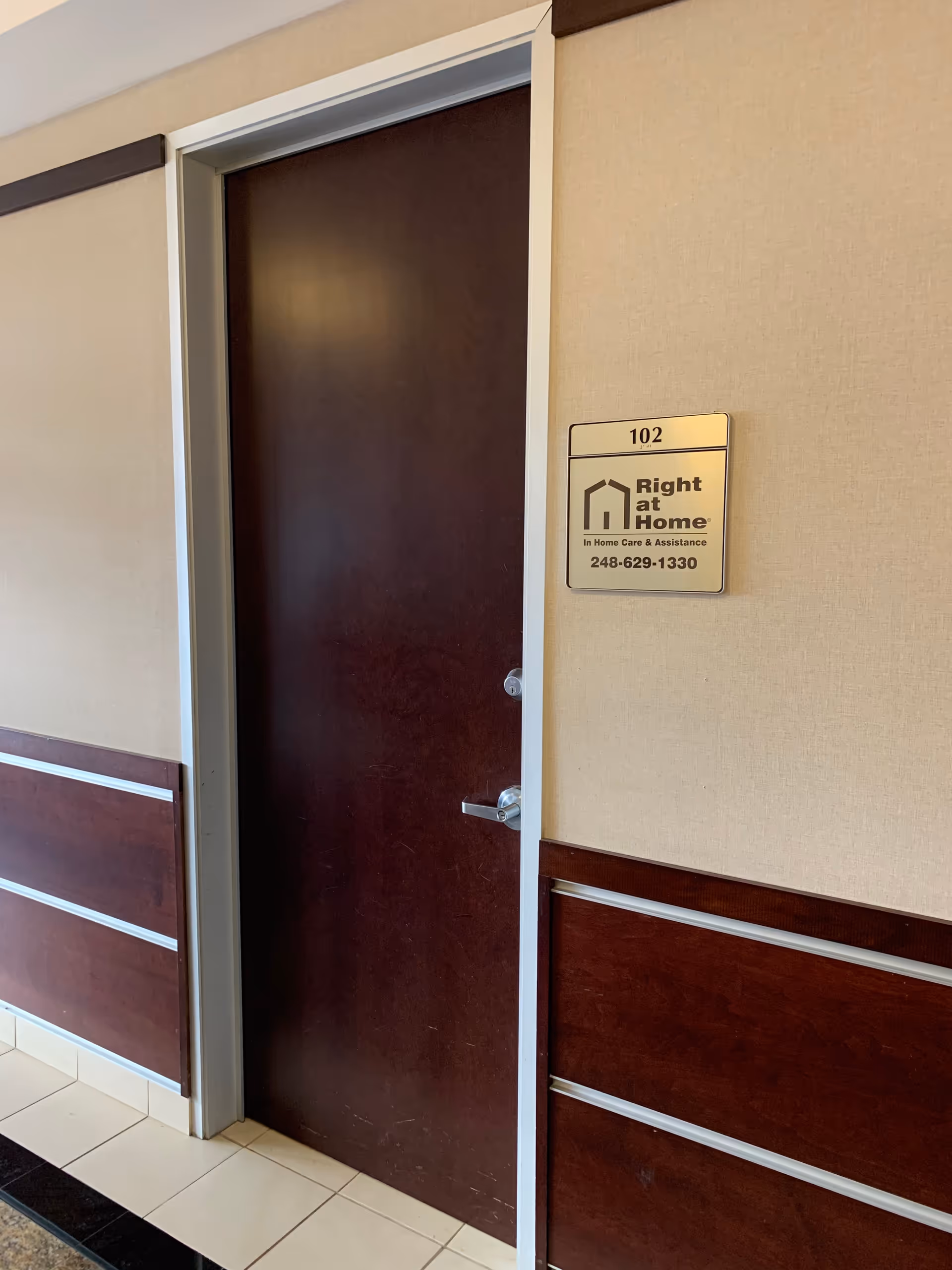 A closed dark brown door labeled 102 with a Right at Home plaque on beige walls.