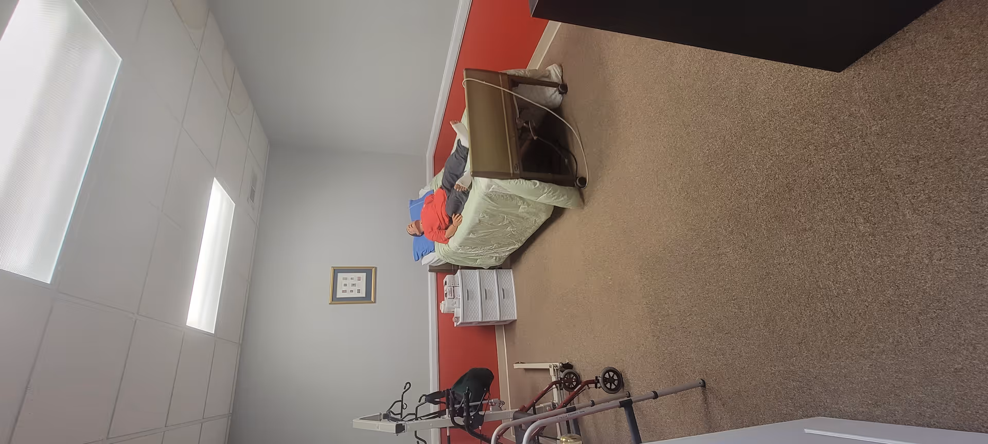 Assisted living bedroom with bed, nightstand, walker, and red accent wall.