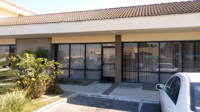 Single-story storefront with glass doors and large windows, a car parked in front.