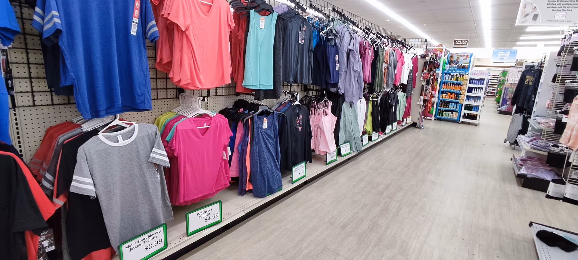 Long aisle of clothing racks in a bright store interior with colorful shirts hanging.