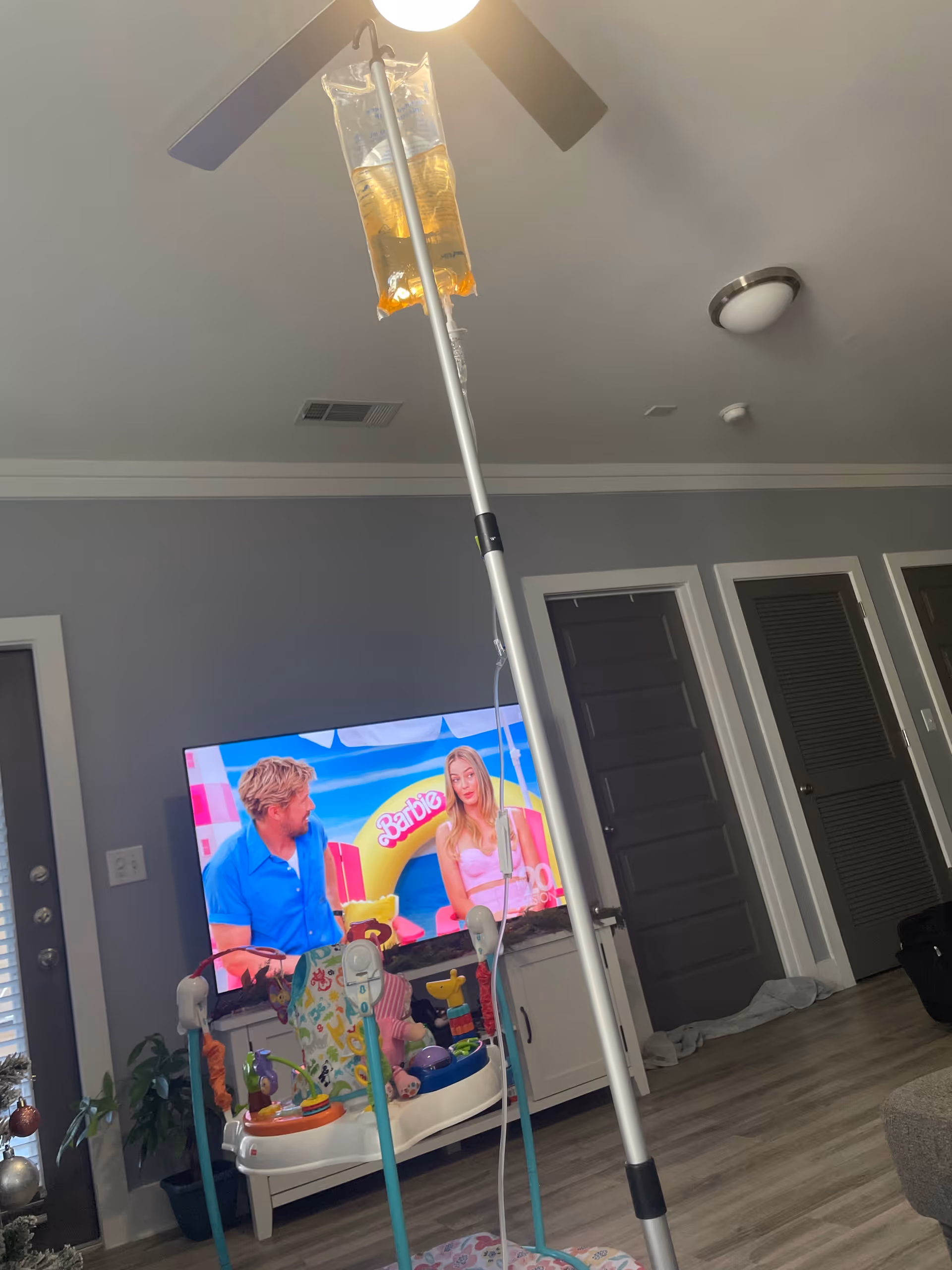 IV pole extends toward a ceiling fan in a cozy living room with TV.