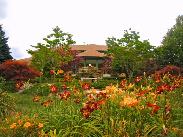 Exterior view of Angela Hospice with a fountain and colorful garden in front.