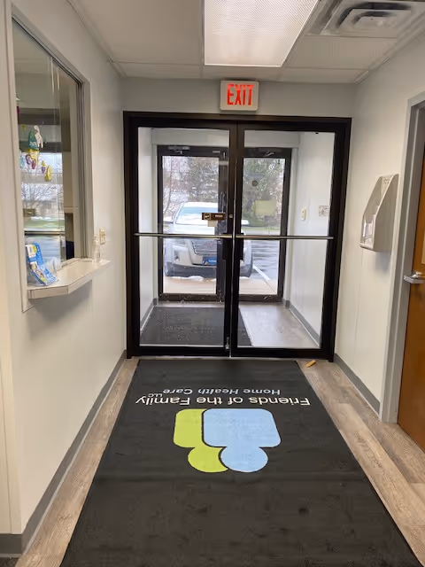 Interior hallway with glass double doors, EXIT sign, and a mat displaying facility branding.