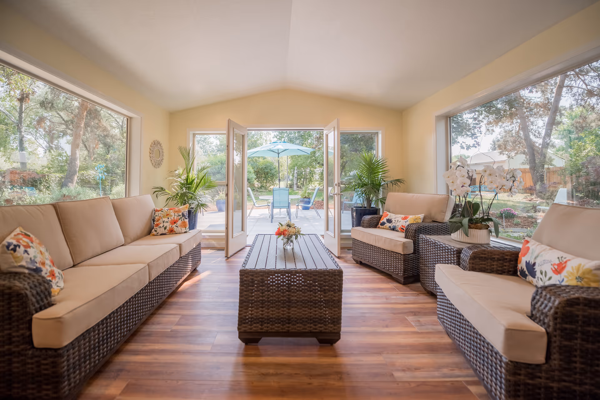 Bright, sunlit indoor living area with wicker couches facing an open glass door to the outdoors.