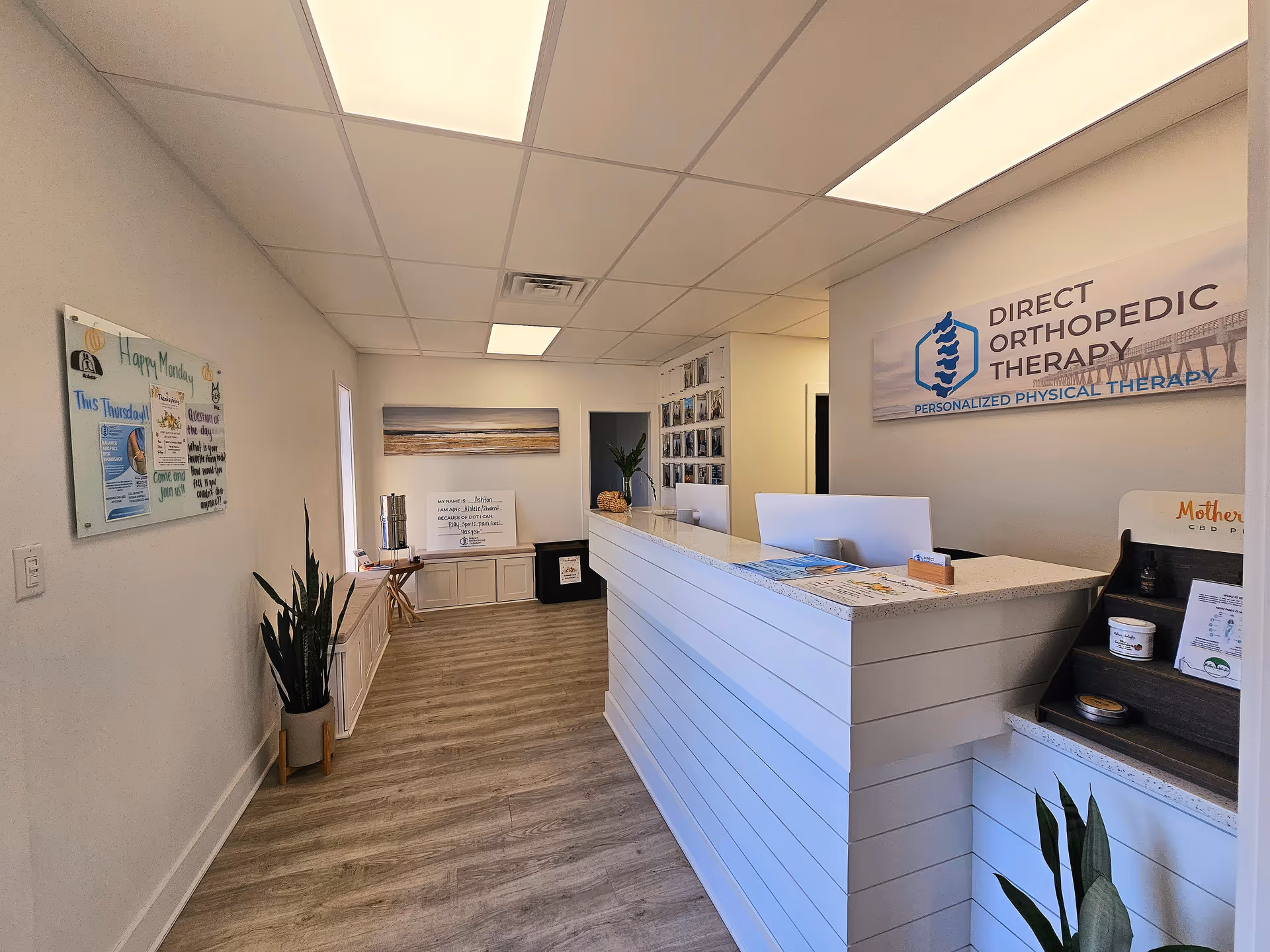 Bright reception area with long white desk, wall sign, plants, and informational posters.